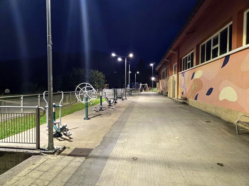 Zona deportiva y parque infantil iluminados de noche, junto a un colegio