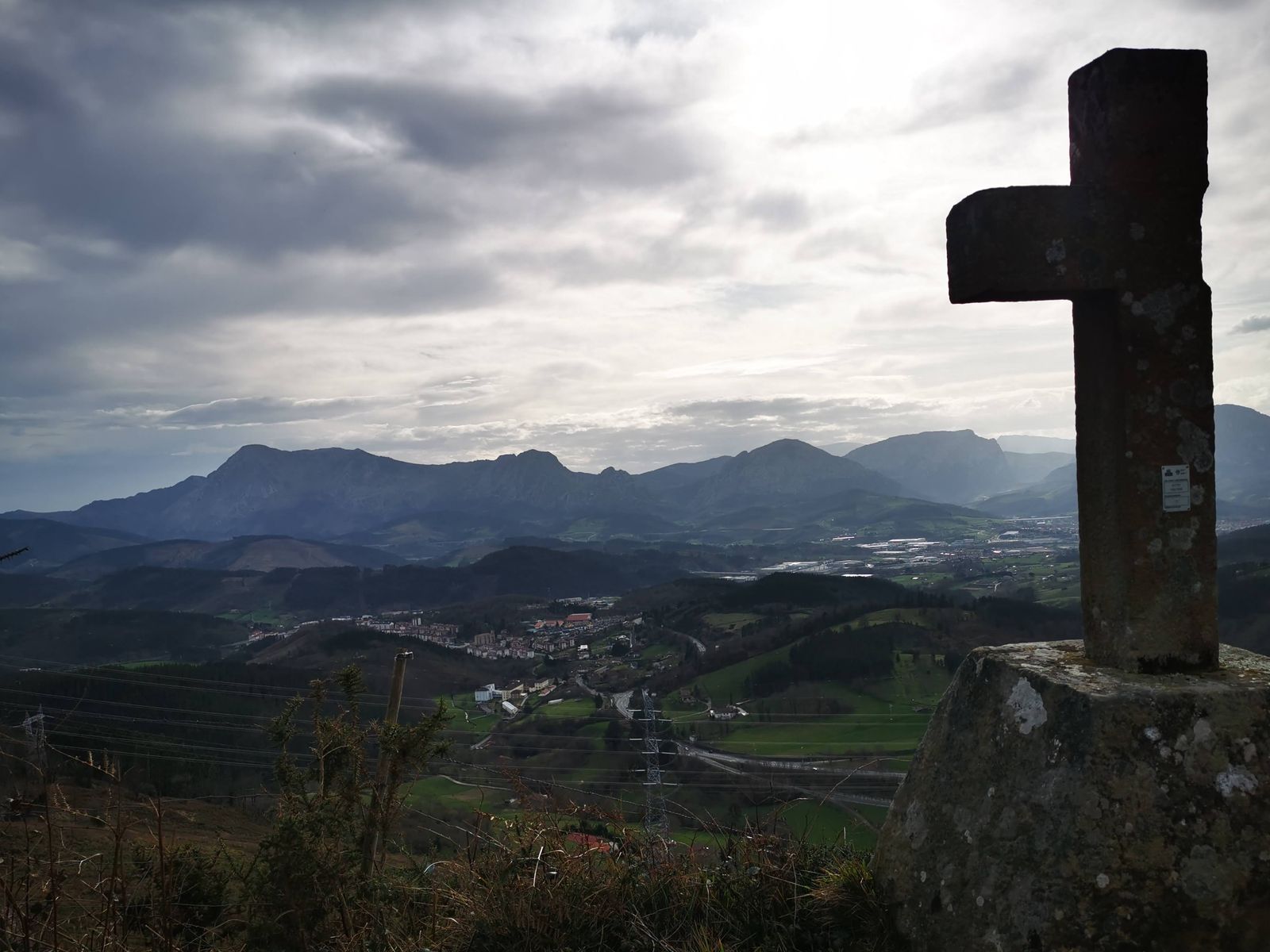 Cruz de piedra a contraluz, con las monta&ntilde;as y el valle al fondo
